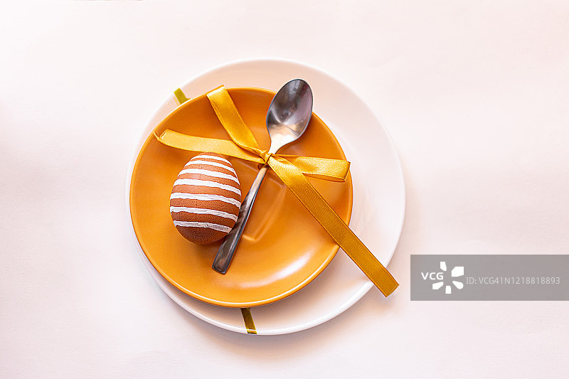 复活节时，在黄白相间的盘子上绘有各种白色图案的棕色彩蛋。带黄色丝带的勺子。传统的东欧文化。俯视图图片素材