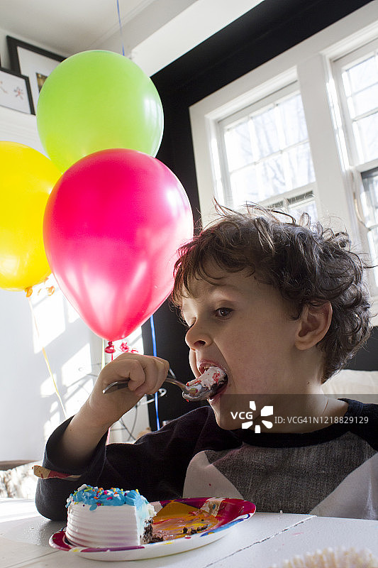 一个棕色卷发棕色眼睛的小男孩在客厅的桌子上庆祝生日，他把蛋糕低角度塞进了嘴巴摄像机图片素材
