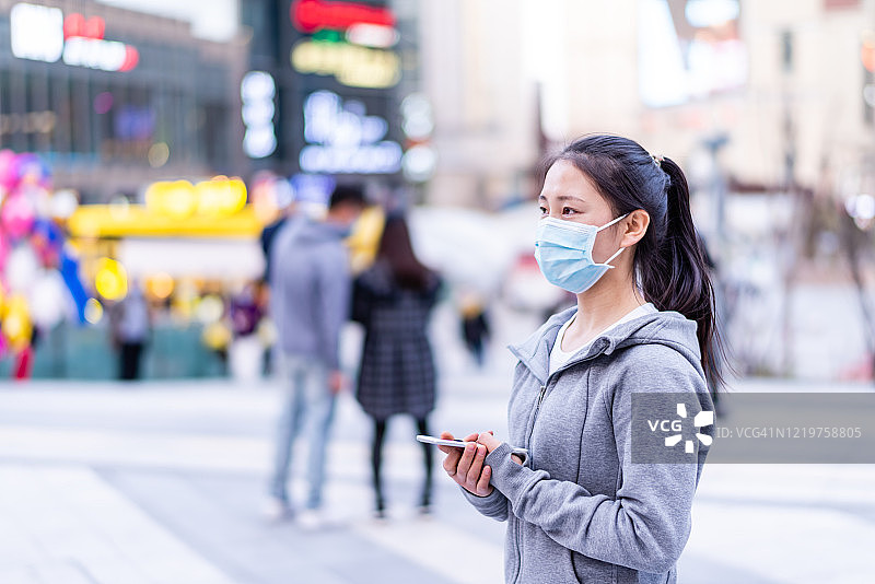亚洲年轻女子戴着口罩在城市街道上传播病毒图片素材