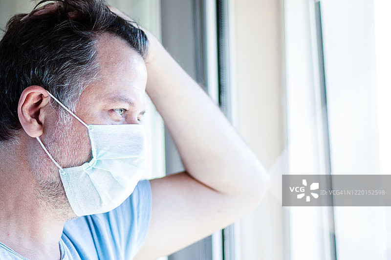 居家隔离中戴口罩的中年病人。他望着窗外。图片素材