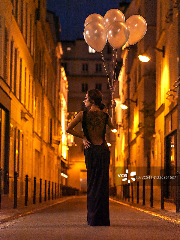 法国巴黎，一名女子晚上拿着气球走在街上图片素材