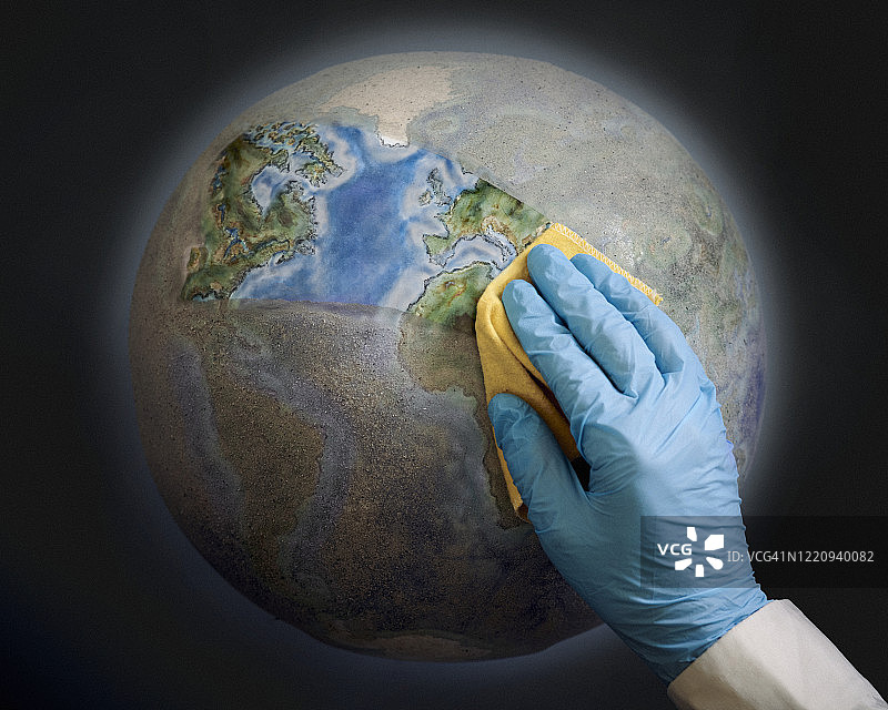 一只戴着蓝色外科手套的手正在清洁肮脏的地球仪。图片素材