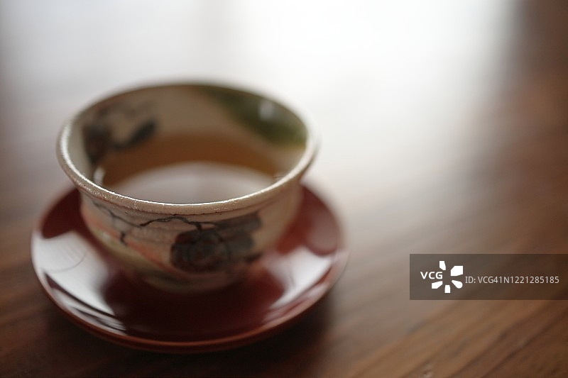 日本的绿茶(煎茶)在一个杯子(Shino-Oribe ware)放在Chataku (Shunkei-nuri木制漆茶杯碟)在木桌上，选择性的焦点图片素材