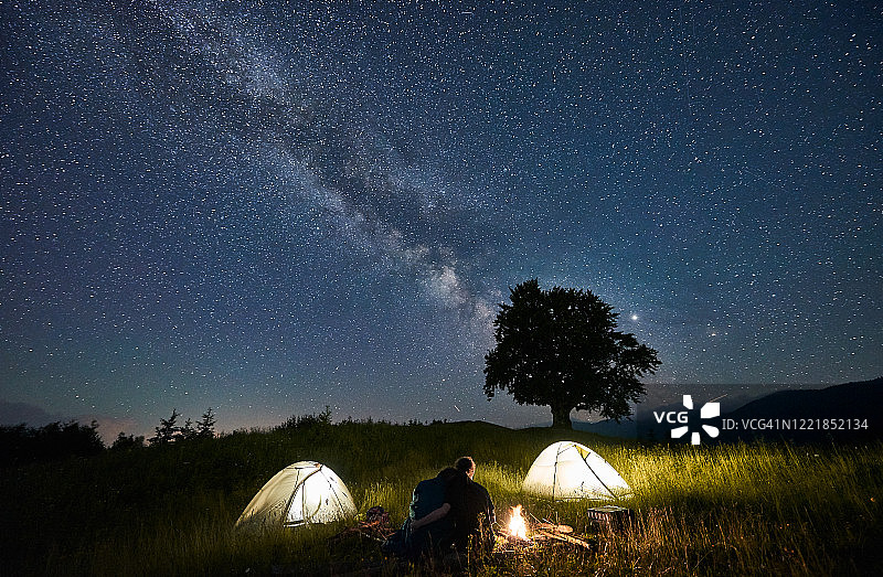 朋友旅行者花时间在山上围坐篝火露营在美丽的星空下图片素材