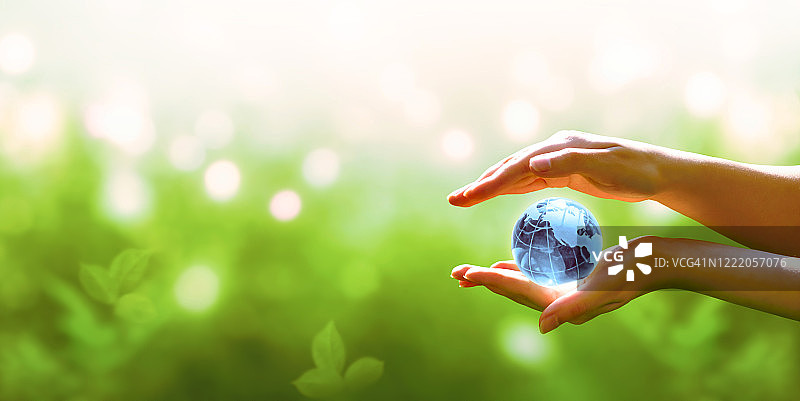 世界地球日卡片。蓝色星球水晶球在人类手中在绿色的背景。节约环境，节约，保护清洁地球和生态，可持续的生活方式理念。图片素材