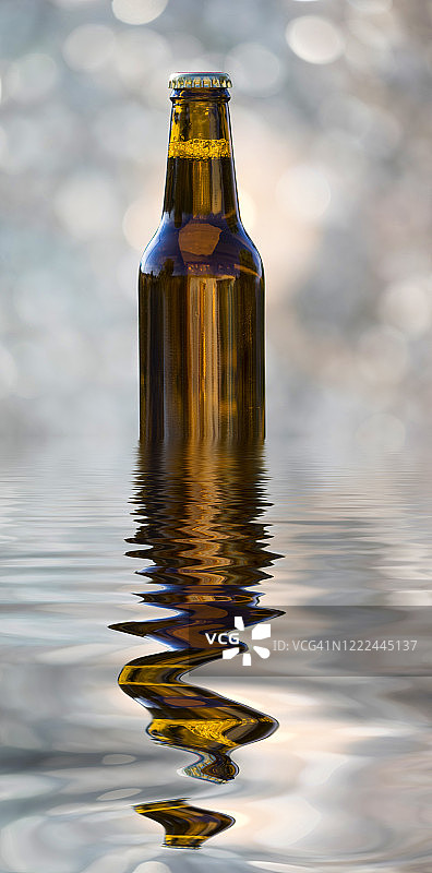 户外的啤酒瓶被阳光照亮，倒映在水面上。图片素材