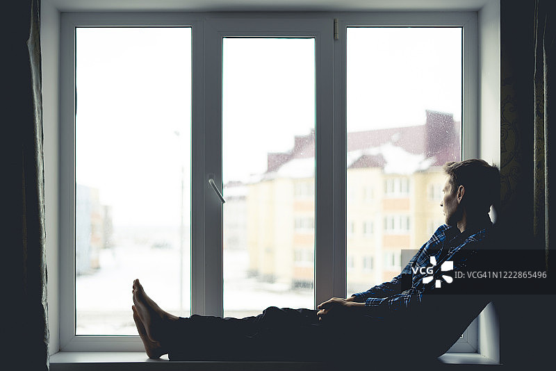 一个忧伤孤独的沉思的男人的剪影坐在窗台上，望着远方的户外，图片素材