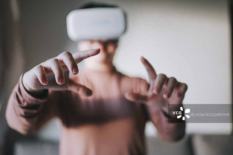 一个亚裔中国中年女性在客厅里使用VR谷歌玩VR虚拟现实在线游戏图片素材