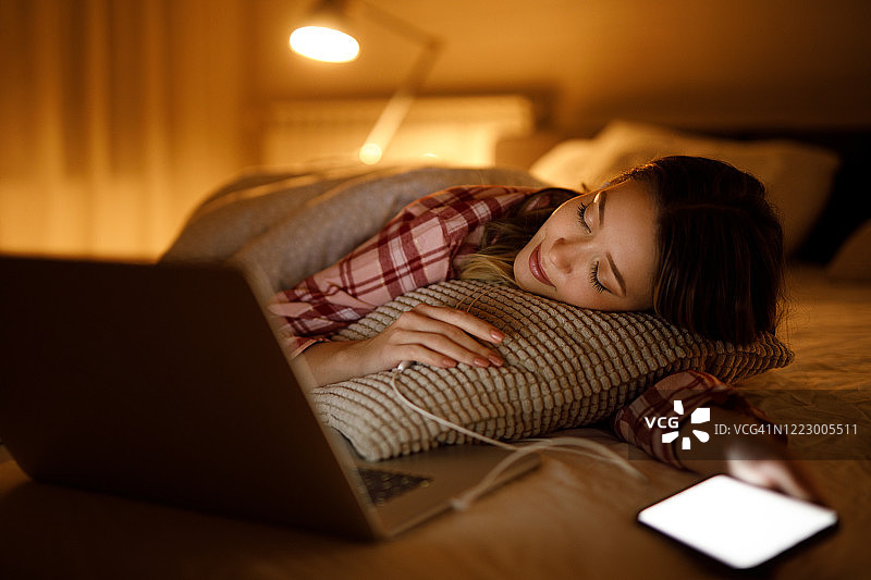 一名年轻女子在家里的笔记本电脑前睡在自己的床上图片素材