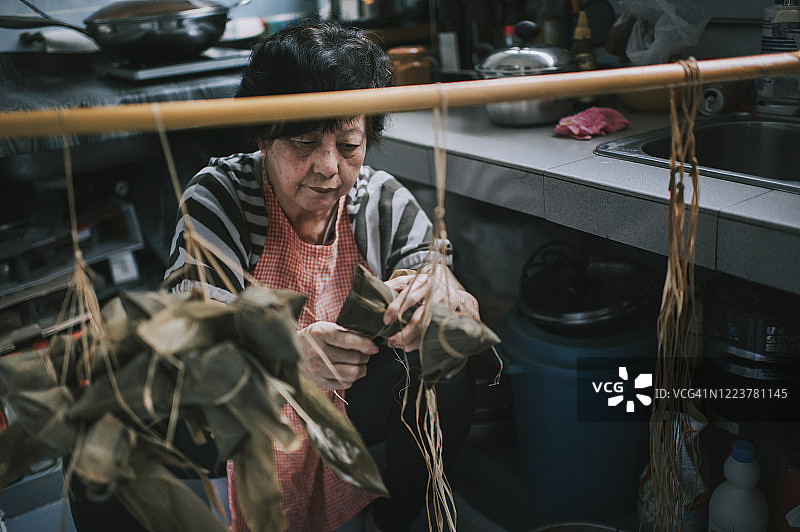 一位年长的亚洲华人妇女在她的厨房里准备粽子，把配料包好，为端午节做准备图片素材