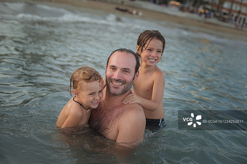 父亲和两个儿子在海滩的水里微笑图片素材