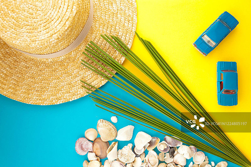 夏季海滩旅游概念。棕榈树叶子，草帽，贝壳，黄色背景上的蓝色汽车图片素材