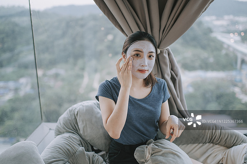 一位亚洲中国美女在卧室里用粘土面具玩得很开心图片素材