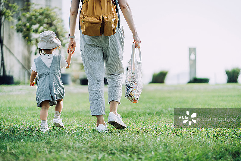 裁剪的镜头，年轻的亚洲母亲携带杂货与棉网生态袋。在杂货店购物后和小女儿手牵手穿过公园。“零浪费”的概念图片素材