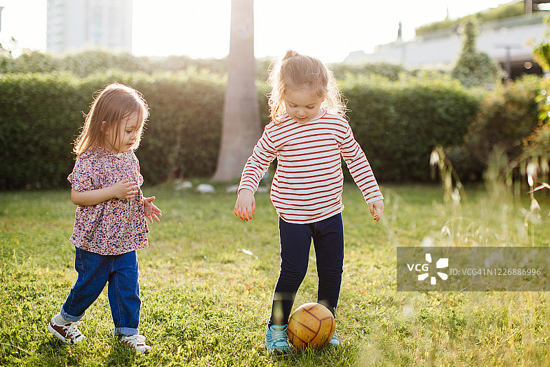 小女孩们在夏天的公园里玩球。孩子和兄弟姐妹在户外玩耍。图片素材