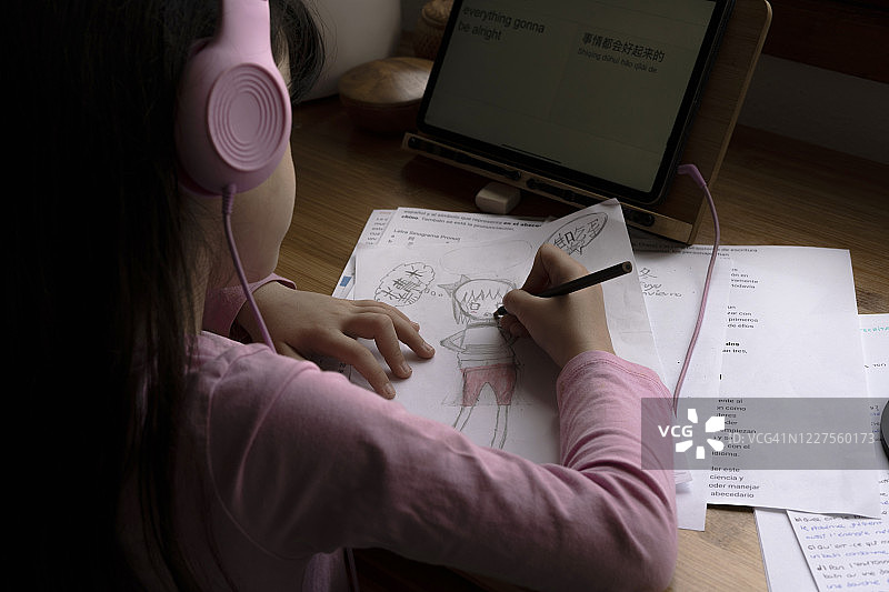 女孩戴着耳机在家里的桌子上用平板电脑画漫画图片素材