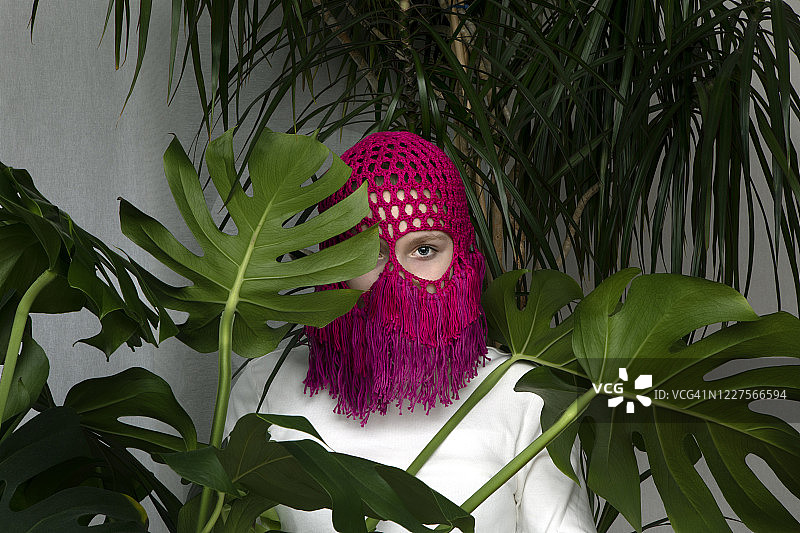 少女的肖像戴着钩针粉红色头饰躲在Monstera树叶后面图片素材