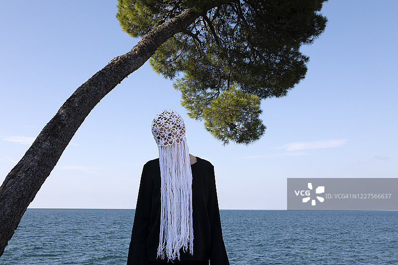 一个女人戴着白色的带流苏的钩针头饰站在大海前图片素材