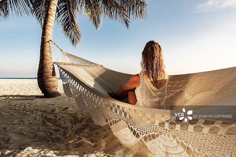 一个女人在沙滩上的吊床上放松。图片素材