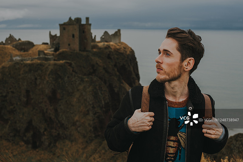 一个年轻人站在苏格兰的邓诺塔城堡前图片素材