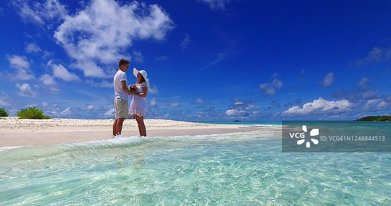 一对浪漫的情侣穿着白色的衣服在加勒比享受蜜月假期，在海边散步，手里拿着一束花在那里度假图片素材