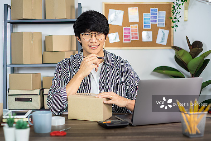 亚洲商人创业中小企业企业家或自由职业者在纸板箱里为客户准备快递盒，在线销售，电子商务，包装和运输的概念图片素材