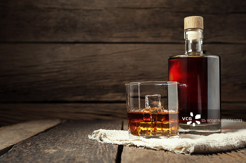 靠近木墙的木桌上放着威士忌酒杯和威士忌酒瓶。图片素材