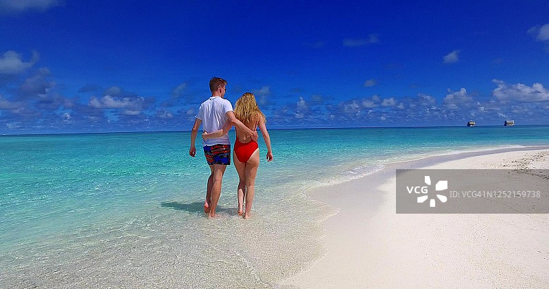 一对年轻的夫妇在白天和他的女朋友沿着原始的海边散步。沙滩假日概念图片素材
