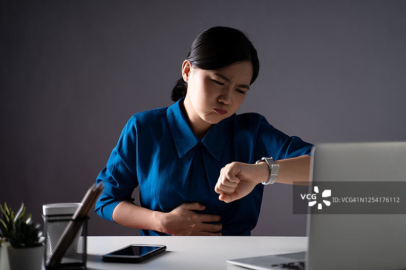 一名身穿蓝色衬衫的亚洲妇女坐在办公室里胃痛。孤立在白色背景上。图片素材