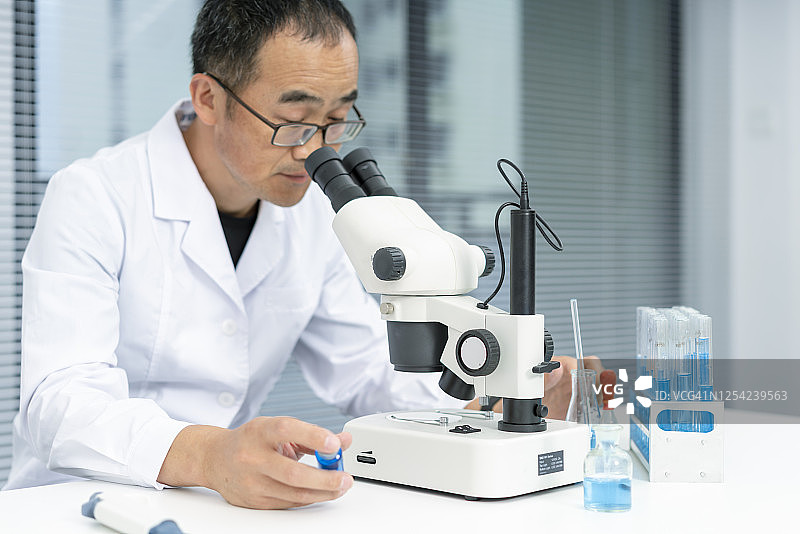 一个亚洲中年男性科学家在观察显微镜图片素材