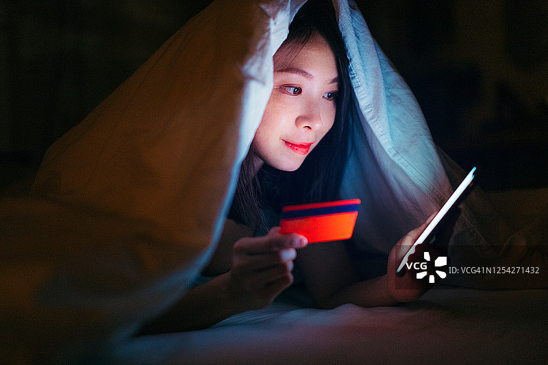 年轻女子在黑暗的床上用智能手机网购图片素材