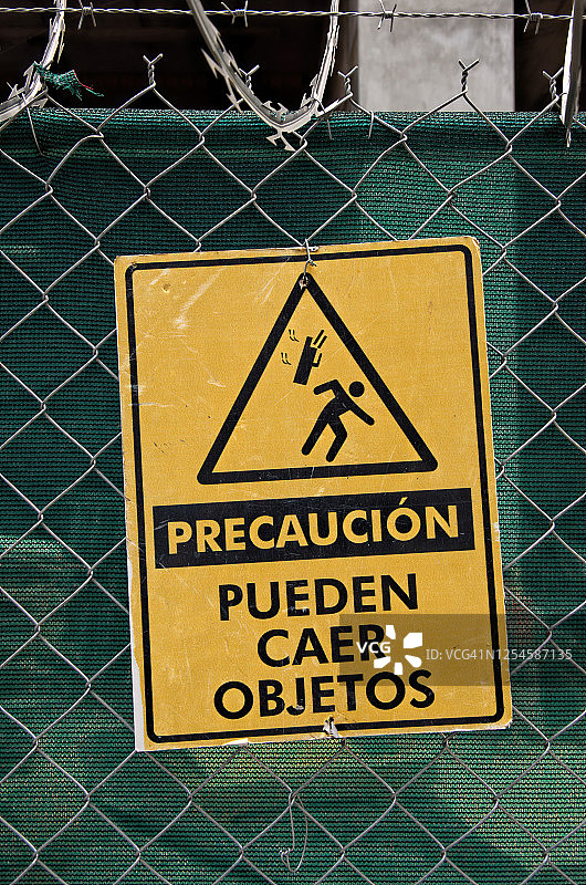 西班牙语警告标志“Precaución: Pueden caer objetos”[警告:物体可能坠落]在建筑工地的围栏上图片素材