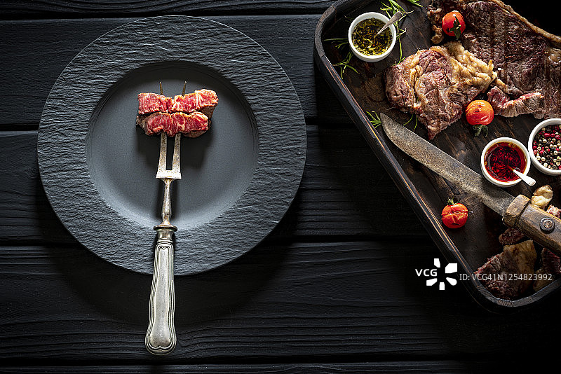 切条牛排上腰牛排牛肉与切肉叉在黑色盘子和木头图片素材