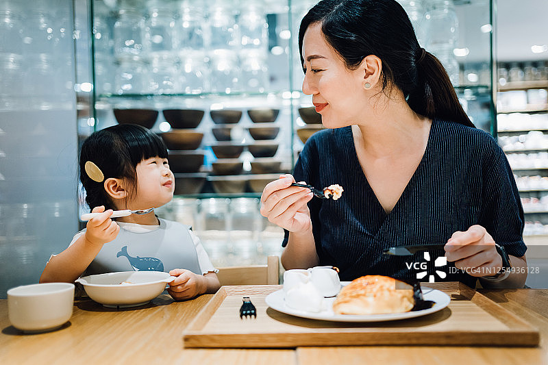 年轻的亚洲母亲和可爱的小女儿在咖啡厅享用甜点。他们互相看着，开心地笑着图片素材