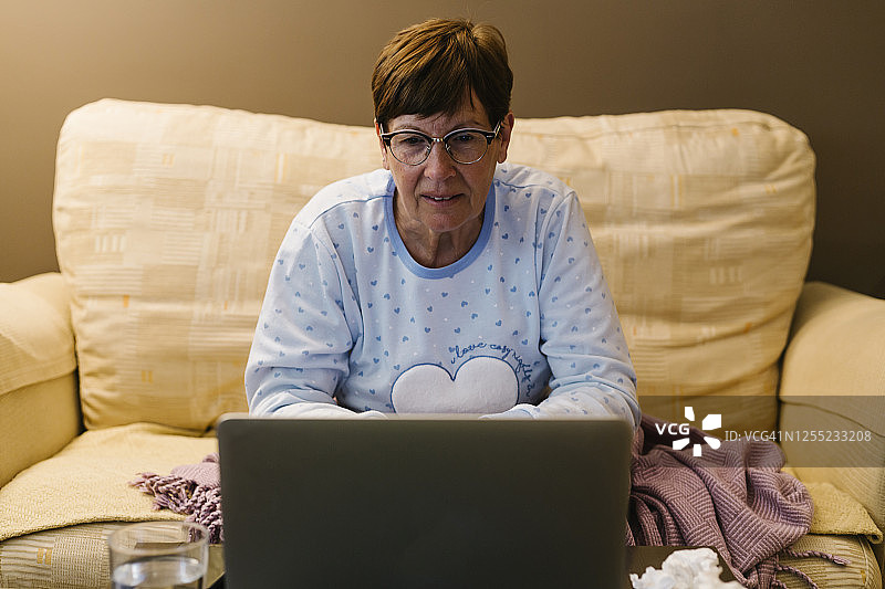 退休的妇女与医生通过视频电话通过笔记本电脑在家讨论疾病图片素材