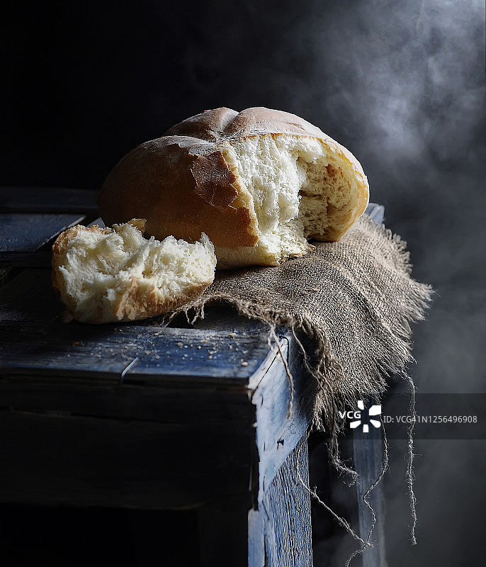 食物摄影的一块白色自制面包与一块布餐巾，侧面的观点，在一个黑色的背景与蒸汽木桌图片素材