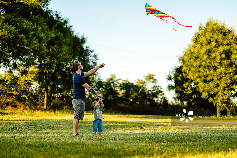 现代父亲教他蹒跚学步的儿子如何在夏日放彩虹风筝图片素材