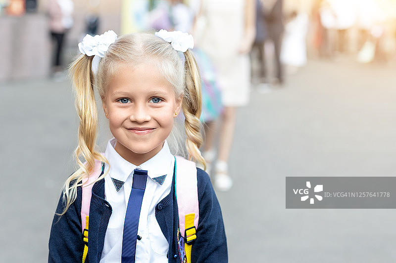 可爱可爱的小白人学校女孩的肖像与滑稽的金发扎辫子，穿着制服和背包享受回到学校。小学一年级初等教育快乐小学生图片素材