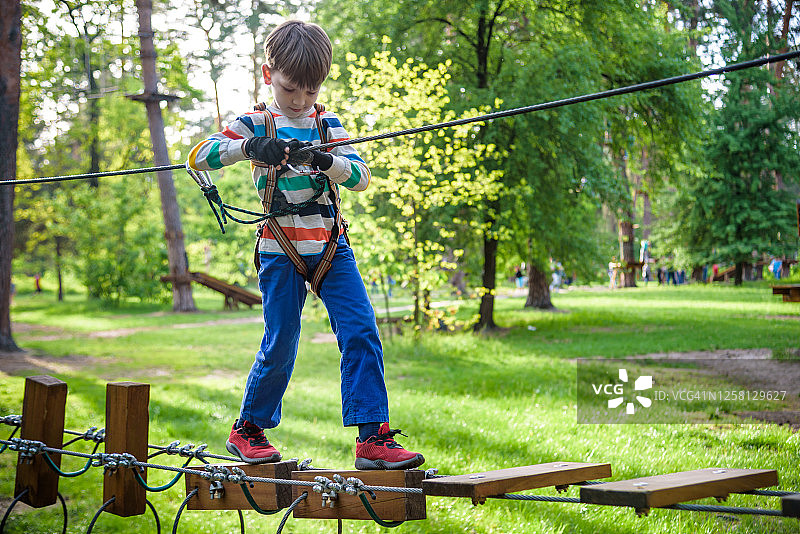 快乐的孩子在冒险公园玩，抓着绳子爬木楼梯图片素材
