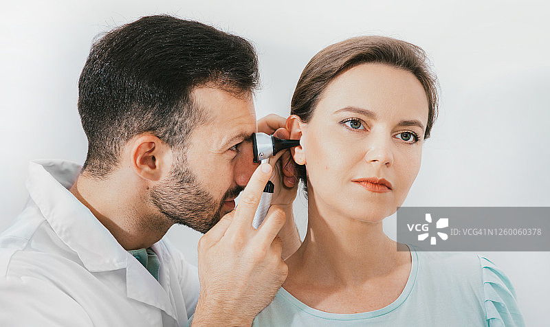 女病人在诊所接受耳朵检查，经验丰富的医生使用耳镜检查女性的耳朵图片素材