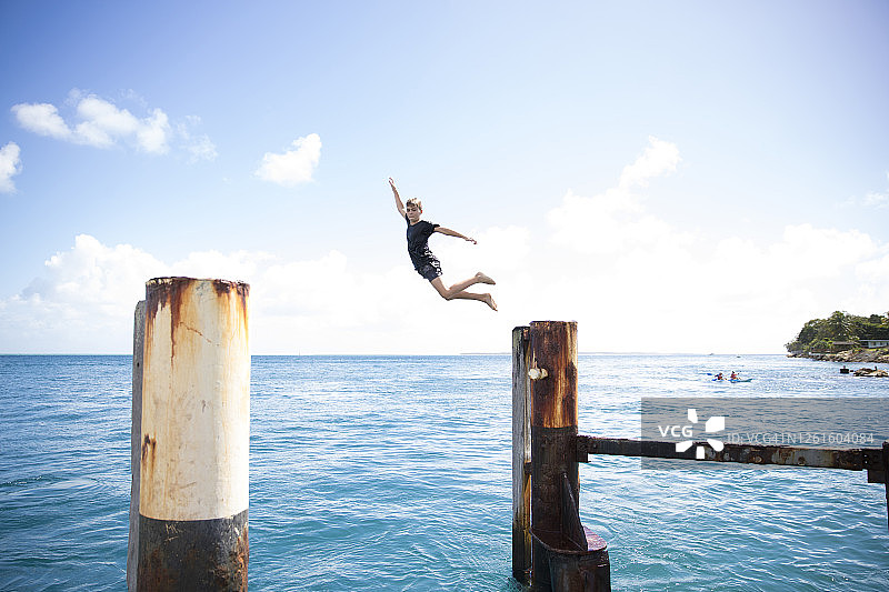 澳大利亚昆士兰，莫尔顿湾，北斯特拉德布鲁克岛，一名男孩从木制码头上跳下图片素材