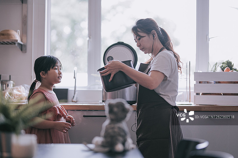 一位亚洲华人母亲在厨房做饭，她的女儿正在用电饭煲煮饭图片素材