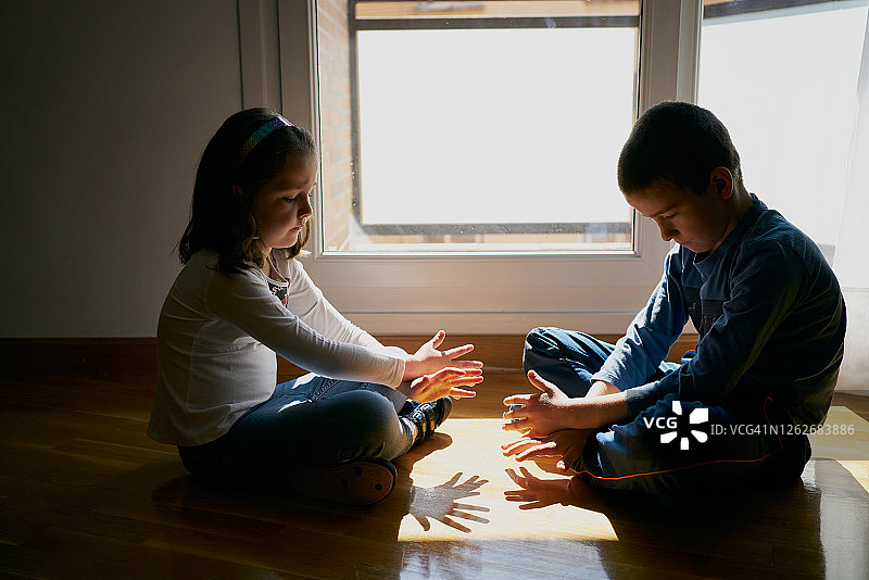 两个孩子坐在地板上，在阴影里玩着他们的手图片素材