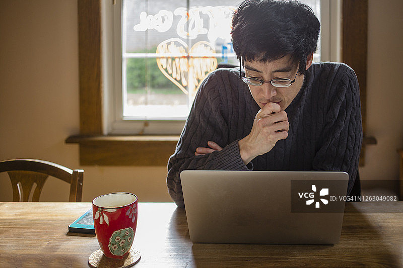 一个男人坐在餐桌前，在电脑上在家工作图片素材