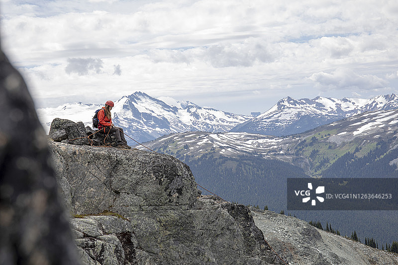 年轻女子登山运动员在山谷上方的岩石丘上做保护图片素材