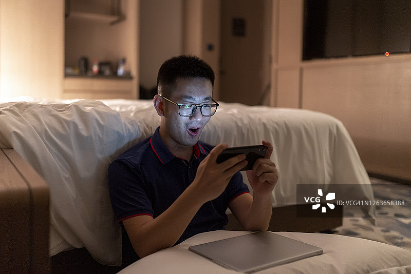 亚洲男人晚上在卧室玩手机游戏图片素材