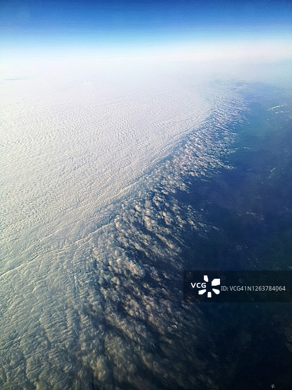 从飞机窗口俯瞰地球的鸟瞰图，可见厚云覆盖，低光和蓝色背景图片素材