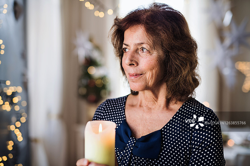 圣诞期间，一位老妇人在室内举着蜡烛的肖像。图片素材