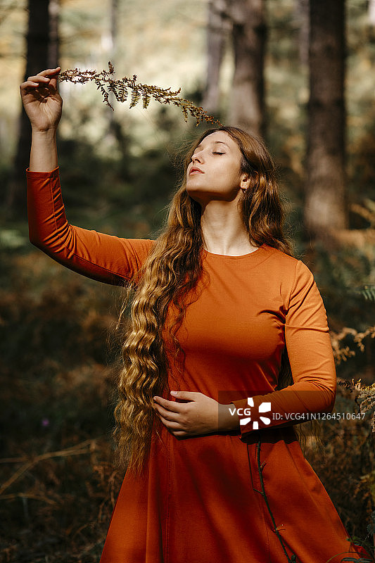 美丽的女人闭着眼睛站在树林里拿着树叶图片素材