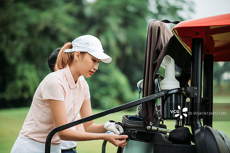 亚洲华人微笑年轻夫妇高尔夫球准备和从后面的高尔夫球车在绿色球场高尔夫球袋图片素材